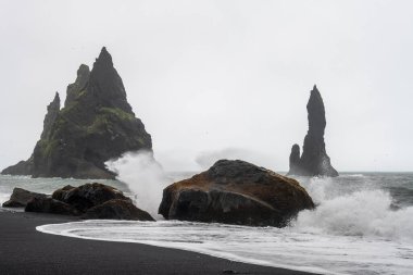 Siyah kumsal Reynisfjara ve Reynisdrangar - İzlanda 'nın güneyindeki Vk Mrdal köyü yakınlarındaki Reynisfjall Dağı' nın altında yer alan bazalt deniz yığınları