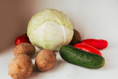 Beyaz arka planda çiğ salatalık, patates, domates ve lahana.