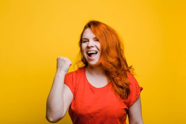 Genç kızıl saçlı kadın evet işareti yapıyor, parlak sarı arkaplan