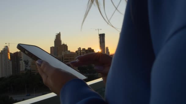 在上午城市的阳台上 女性在智能手机上输入信息的特写镜头 背景为日出的城市场景 — 图库视频影像