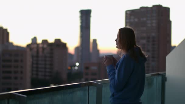 女性は熱いお茶とコーヒーで一日を始めます 彼女は暖かい飲み物を楽しみ 朝の空に対して高い建物と都市のシーンを見て — ストック動画