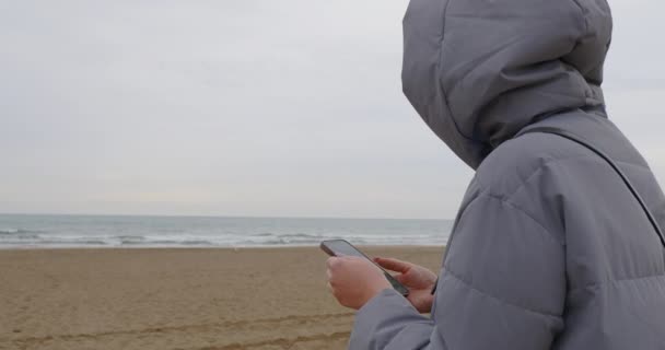 Donna Giacca Con Cappuccio Utilizzando Telefono Sulla Spiaggia Vuota Lei — Video Stock