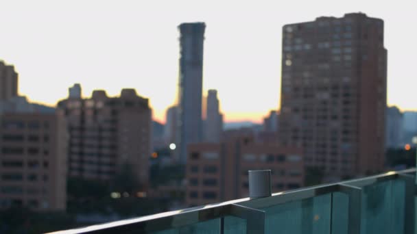 上層階のバルコニーのレールの上に熱いお茶やコーヒーのマグカップ 背景に朝の空を背景に高層ビルが建ち並ぶ街並 — ストック動画
