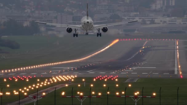 滑走路の夕方の空港に乗客の飛行機が着陸し 明るく駐車灯で照らされ 街の住宅ビルの背景を背景に — ストック動画