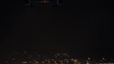 Yan ışıkları açık bir yolcu uçağı, gece kareyi geçen siyah bir gökyüzünün arka planına iniyor.
