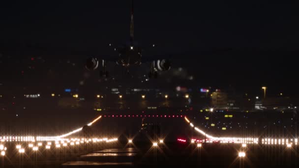 乗客の飛行機は 夜空を背景に 空港で飛行機を動かし 家で輝く窓を背景に 明るい滑走路に夜に着陸します スイスのチューリッヒ — ストック動画