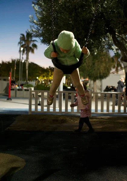 女の子は街の公園でスイング 落下から守るために特別なコーティングを施した遊び場でスイングします — ストック写真