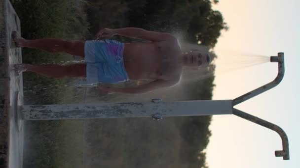 수직으로 천천히 파란색 트렁크 남자가 샤우어 밑에서 정면으로 하늘을 배경으로 — 비디오