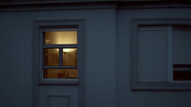 Outside view of the house window in the dusk. Empty room with dim light of a floor lamp. Atmosphere of quiet evening