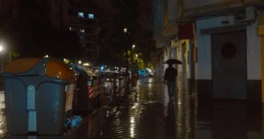 A man with umbrella walking along the deserted street in residential district. Drizzling rain in night city