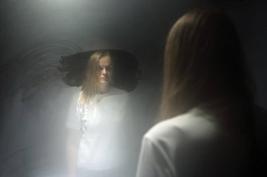 Blond woman in the reflection of sweaty mirror. Female in white t-shirt staring at herself with blank look. Age crisis