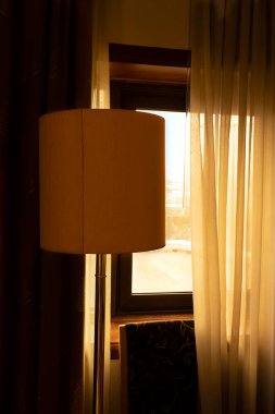 Room details in warm morning sunlight. Floor lamp and chair near the window with half open curtains
