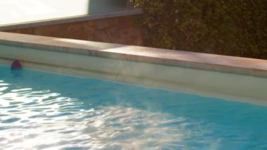 Slow motion static shot of steam rising from rippling hot water in pool on sunny summer day