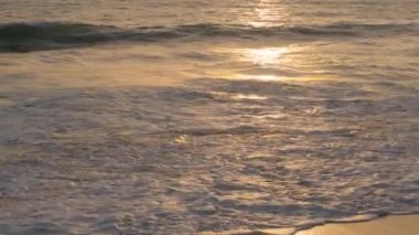 Sunset over ocean, waves wash sand beach