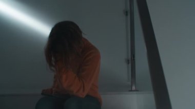 Bir evin içinde merdivenlerde oturmuş telefonundan video seyretmeye dalmış bir gencin orta boy fotoğrafı. Uzun saçları yüzünü kapatıyordu. Dikkatlice ekrana odaklandığını görüyoruz.