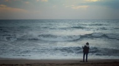 A boy is seen dancing on the shore of the ocean to his own rhythm in the evening. The boy is slightly out of focus for a more dreamy look