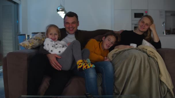一个由四个人组成的高加索家庭晚上在沙发上看电视 40多岁的父母 12岁的儿子和5岁的女儿 — 图库视频影像