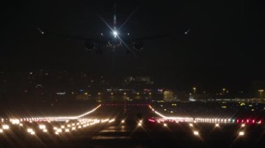 Bir uçağın karanlık bir silueti iniyor ve geceleyin bir havaalanındaki piste iniyor.