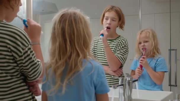 鏡の前で電気歯ブラシで歯を磨く兄と妹 — ストック動画