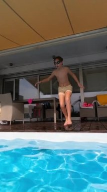 Dikey video - yavaş çekim - güneşli bir yaz günü ferahlatıcı bir villaya atlarken yüzme gözlüğü takan 12 yaşında bir çocuk. Kamera onu suyun altında takip ediyor, onu yakalıyor.