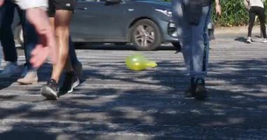 Yaya ayaklarının caddeden karşıya geçerken aralarında süzülen sarı bir balon olan zebra geçidinde, arabalar hareket etmeye devam ettikçe balon havaya savruluyor ve havaya karışıyor.