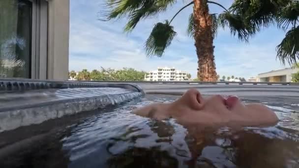 12歳の少年が屋外のホットタブで顔を上げ 暖かい水の下で顔のほとんどを水没させ 癒しの経験と休暇の時間を楽しんでいる様子を間近で見ることができます — ストック動画