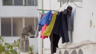 Renkli giysiler, güneşli bir yaz gününde, beyaz bir evin duvarına asılıp kurumaya bırakılır.