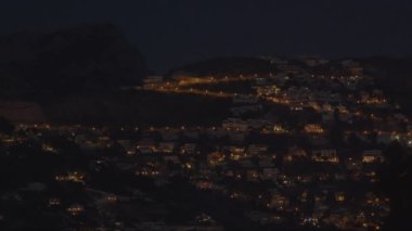 İspanya 'da bir tepenin üzerinde küçük bir gece şehri. Evlerin parlayan ışıkları karanlık mavi gökyüzüne karşı ağaçlar oluşturur.