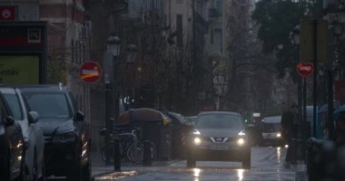 VALENCIA, İSPA - 13 Mart 2023: yağmurlu bir sabahta ışıkların loş ışığı altında şemsiyeli insanlar karşıya geçiyor