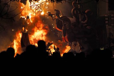 Valencia, İspanya 'daki Fallas kutlamaları sırasında ışıklarla aydınlatılan bir sokakta Ninote bebeklerinin tutuşmasını izleyen insanların yatay fotoğrafı.