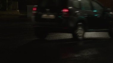 Yağmurdan sonra, gece ıslak banliyö yolunda arabalar sürüyorlar, farlarıyla yolu aydınlatıyorlar.
