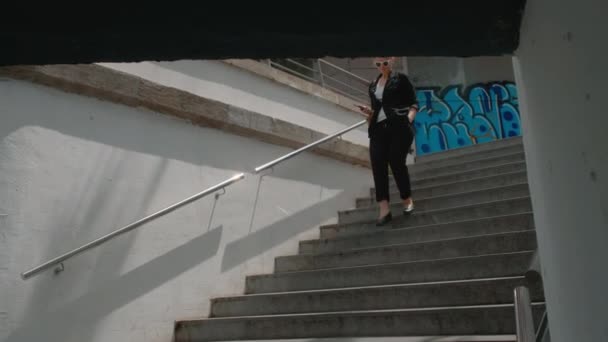 黒いスーツの若い女性が地下の歩道に降りてきて携帯電話で何かを読んでいる — ストック動画