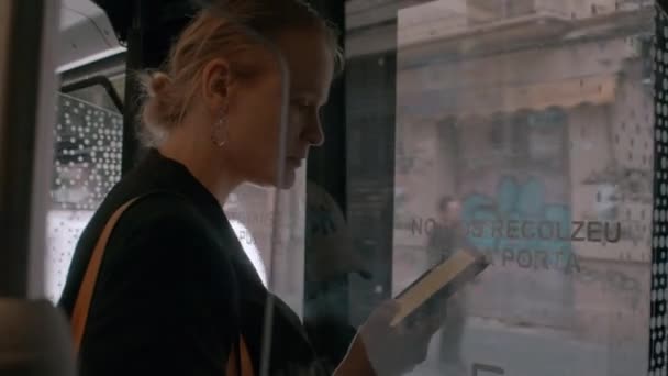 バスのドアの近くに女性が立っていて 手に電子書籍を持っていて 市バスに乗っている間にそれを読んでいます — ストック動画