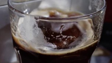 Yavaş çekimde, bir bardak kahveye buz koyan birinin eli.