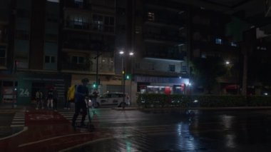 VALENCIA, İSPA - 23 Mayıs 2023 akşamı, yağmurdan sonra, yaya geçidinde birkaç yaya geçidi, bir yiyecek teslimatçısı, sarı sırt çantalı bir motosikletle geçerken,