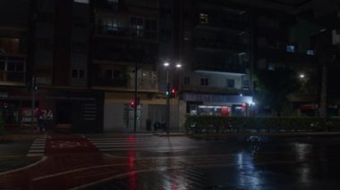 VALENCIA, SPAIN - 23 Mayıs 2023: yağmurdan sonra yağmurlu asfaltta seyrek arabaların sürdüğü terk edilmiş gece şehrinin sokakları. Evlerin pencerelerinde ışıklar sönüyor, Valencia, İspanya
