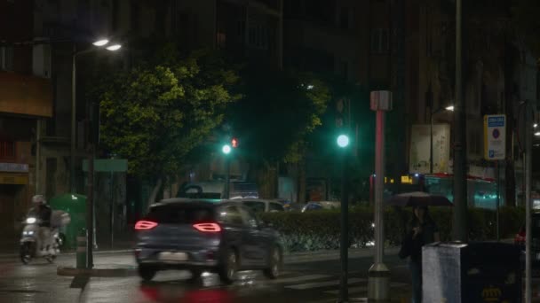 バレンシア スペイン 2023年5月23日 女性がバス停で待っていて 雨から傘で身を隠している 街灯はぬれた道を照らす 交通信号が明るくなり — ストック動画