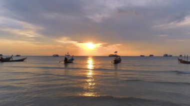Koh Tao üzerinde renkli gün batımı, okyanusta kayıklar, akşam ışığı kıyıları aydınlatıyor, büyüleyici deniz manzarası.