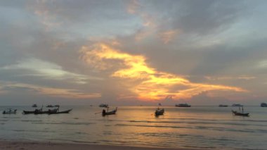 Durgun sularda renkli teknelerle Koh Tao 'nun üzerinde canlı bir günbatımı. Akşam ışığı kıyı şeridini yıkarken çarpıcı bir deniz manzarası yaratır..