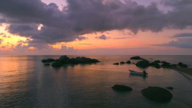 Tayland, Koh Tao 'daki Sai Nuan Sahili' nde renkli günbatımı manzarası. Tekne denizde yüzüyor, muhteşem kaya oluşumları var. Gece Tayland sahilinin güzelliğini tecrübe et..