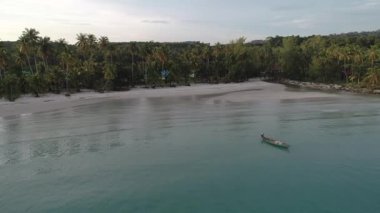 Koh Kut, Tayland 'da kumlu bir sahilde bir tekne. Dalgalar kıyıya çarpıyor ve tekne huzur içinde dinleniyor. Manzara güzelliği dingin atmosfere katar.