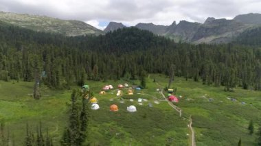 Rusya 'daki Sibirya tatil kampının havadan görünüşü. Destansı bulutları, yeşil tarlaları ve görkemli dağlarıyla göz kamaştırıcı doğal manzara. Sakin göl ve eğimli ağaçlar romantik bir zemin oluşturur. İdeal
