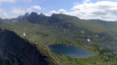 Sibirya dağlarının çarpıcı hava görüntüleri. Yuvarlanan tepeler, yeşil çayırlar, görkemli zirveler, destansı bulutlar ve açık mavi bir gökyüzü..