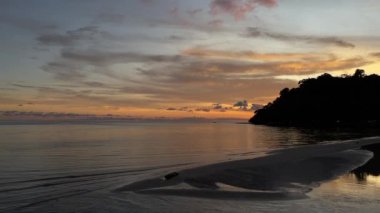 Tayland sahillerinde çarpıcı bir tropik gün batımı. Güneş okyanusun üzerinde batarken gökyüzünü canlı renkler kaplıyor. Dramatik bulutlar güzel bir zemin yaratır..