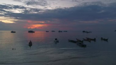 Güzel Tayland gün batımı akşam ışığını yansıtan renkli bulutların üzerinde. İnsanlar kıyı şeridinde teknelerle çevrili tatilin tadını çıkarıyor. Koh Tao deniz manzarası ve oteller güzel manzaralar yaratır..