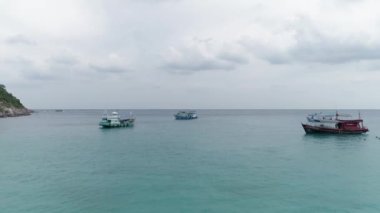 Koh Tao, Tayland 'da dramatik bir gün batımı. Gemiler fırtına bulutlarının altında körfezde. Gemilerin canlı renkleri ve büyüleyici gökyüzüne karşı kıyı şeridi. Fırtına bulutlarının ortasında gemilerle deniz manzarası.