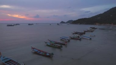 Renkli teknelerin üzerinde nefes kesen gün batımı Koh Tao kıyısı boyunca yol alıyor. Pahalı plajları ve büyüleyici deniz manzarasıyla bilinen bir Tayland adası..