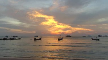 Deniz üzerinde canlı bir gün batımı. Tekneler, bulutlar ve renkli bir gökyüzü. Bir Tayland adası olan Koh Tao 'nun kıyı şeridi sıcak akşam ışığı ile aydınlanır. Gemiler okyanusu dolduruyor, güzel bir deniz manzarası yaratıyor.