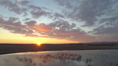 Kırmızı bulutlar, yeşil çimenler, bir göl ve manzarayla baş döndürücü bir gün batımı. Pembe ışınlar gökyüzünü dolduruyor, büyüleyici bir sahne yaratıyor..