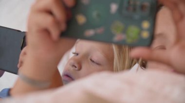 Genç bir kızın akıllı telefon ekranını dikkatle izlemesini ve kardeşinin de aynı şeyi bulanık bir ön planda yapmasını.